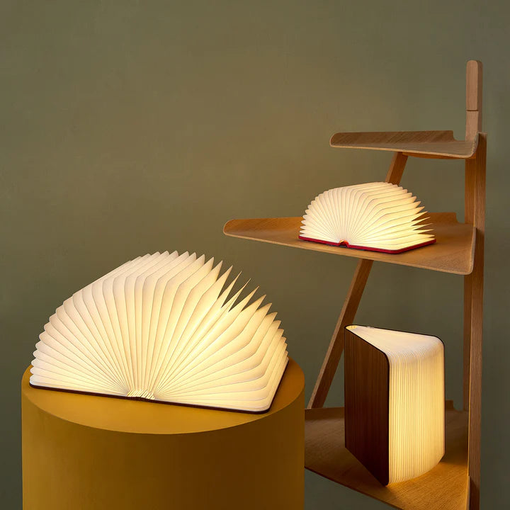 Foldable book-shaped lamp on a small table with shelves in the background